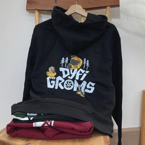 Black hoodie with "Dyfi Groms" logo on a wooden stool against a white wall.